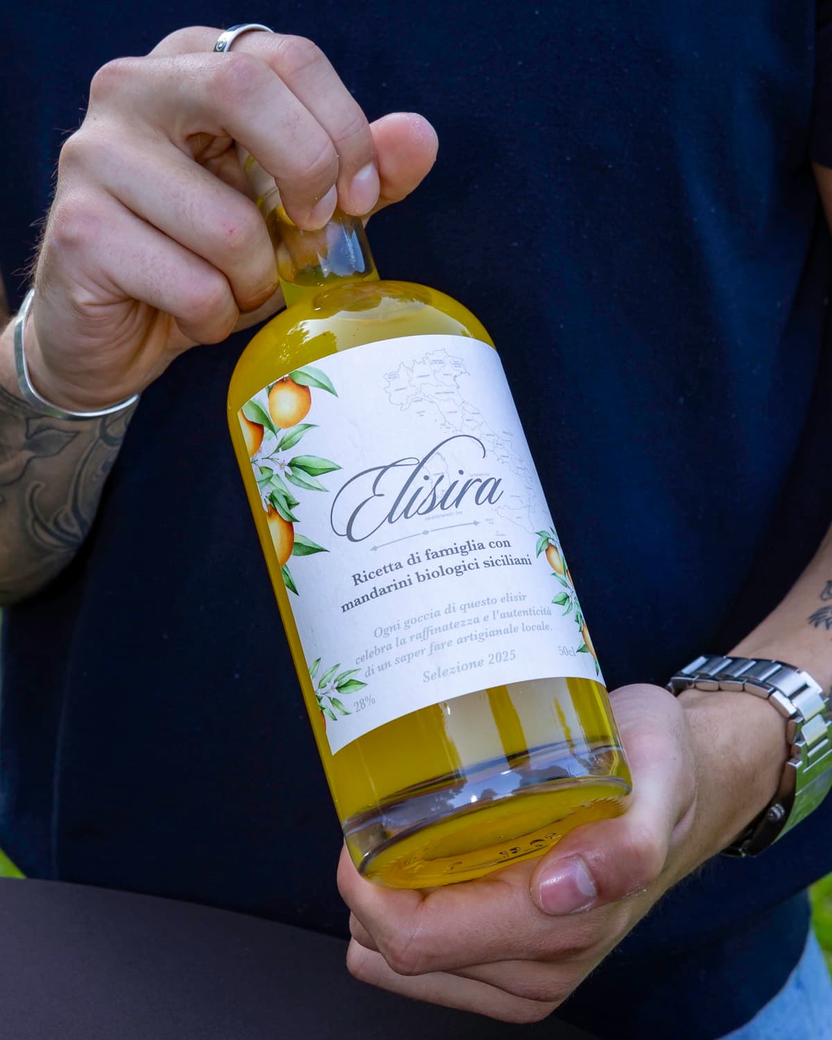 Une bouteille d'Elisira 50 cl présentée à deux mains, étiquette de face