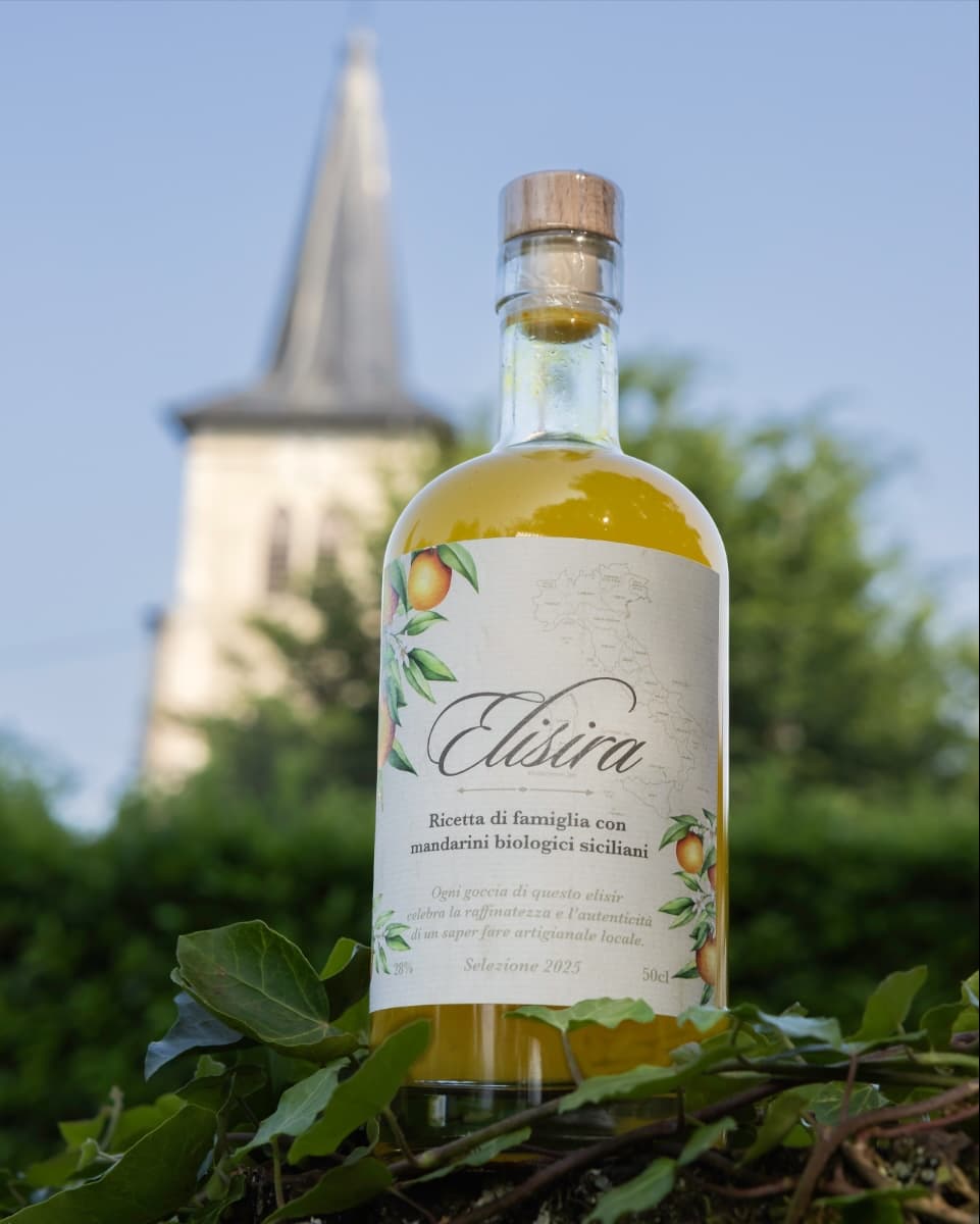 Bouteille d'Elisira 50 cl posée sur du lierre, un clocher de village derrière
